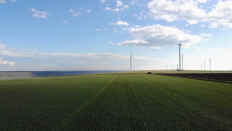 Niedrige-Antenne-Durch-Grüne-Felder-Mit-Windkraftanlagen-An-Sonnigen-Tagen
