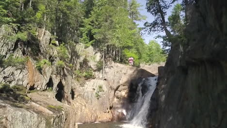 male hiker standing next to a waterfall in slow motion at small falls in the maine wilderness