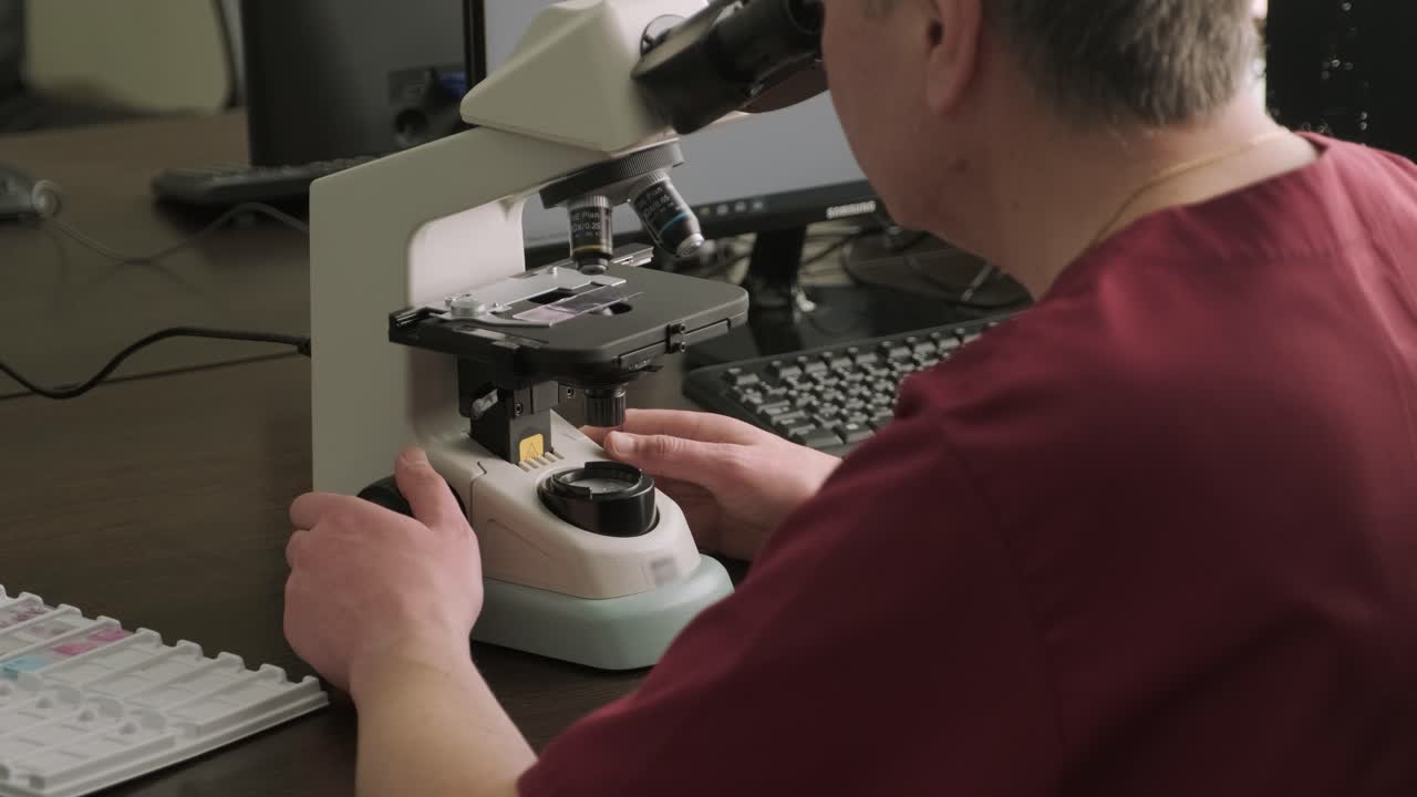microbiólogo masculino, trabajador médico mira una muestra de sangre a través de un microscopio, hace análisis en el laboratorio. asistente de laboratorio lleva a cabo una investigación histológica de biomateriales utilizando un microscope moderno
