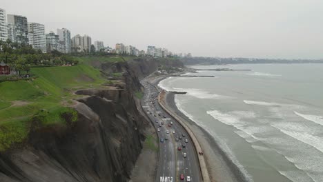 El-Dron-Amplía-La-Lente-Sobre-Miraflores,-Lima:-Carretera-Costera,-Torres-De-Viviendas-En-Lo-Alto-Del-Acantilado.