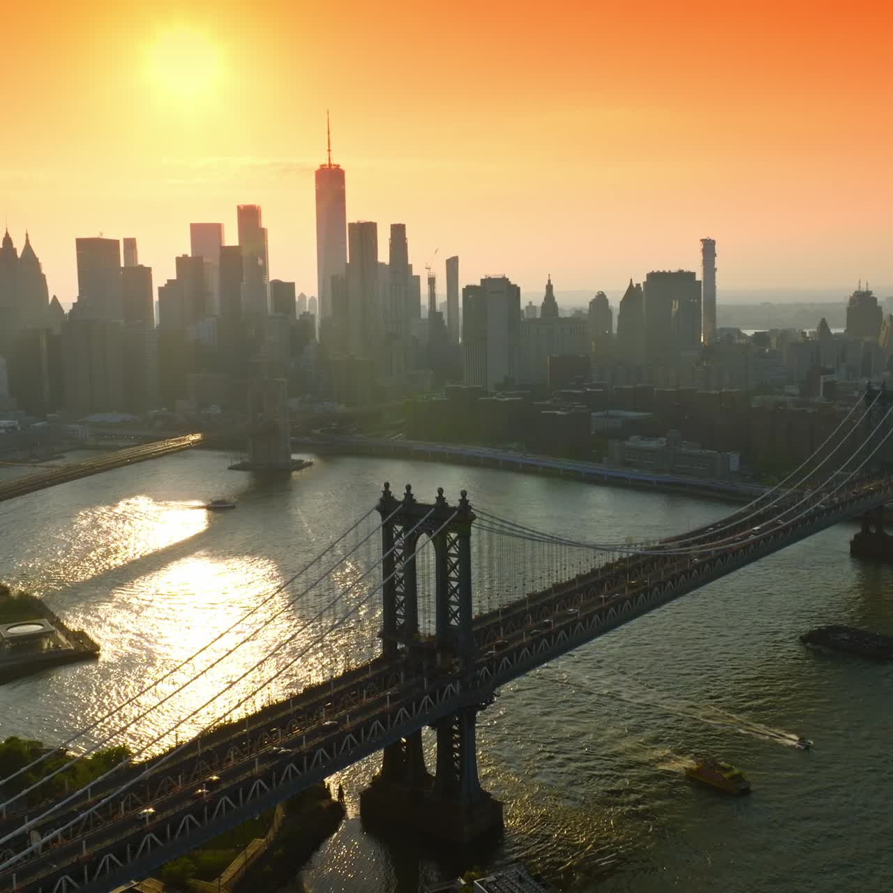 Lively traffic over Manhattan Bridge at Golden hour. Gorgeous skyscraper's silhouettes at backdrop of orange skies. Top view