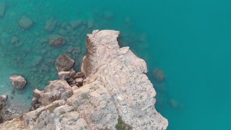 birds eye drone footage of rocky cliff edge, as camera soars over rugged landscape of blue water and white stone wall