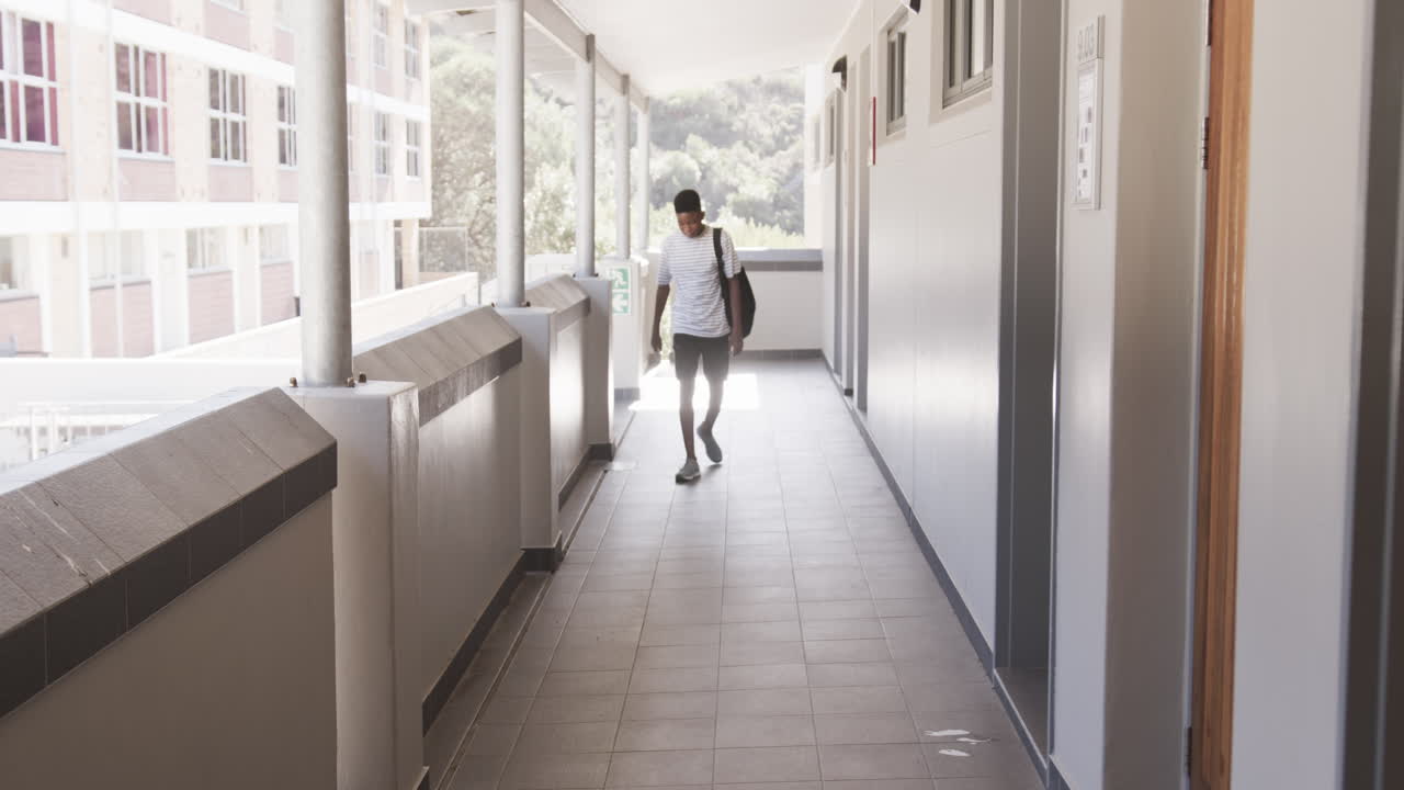 Walking in school hallway, African American teenage boy in casual clothes looking down