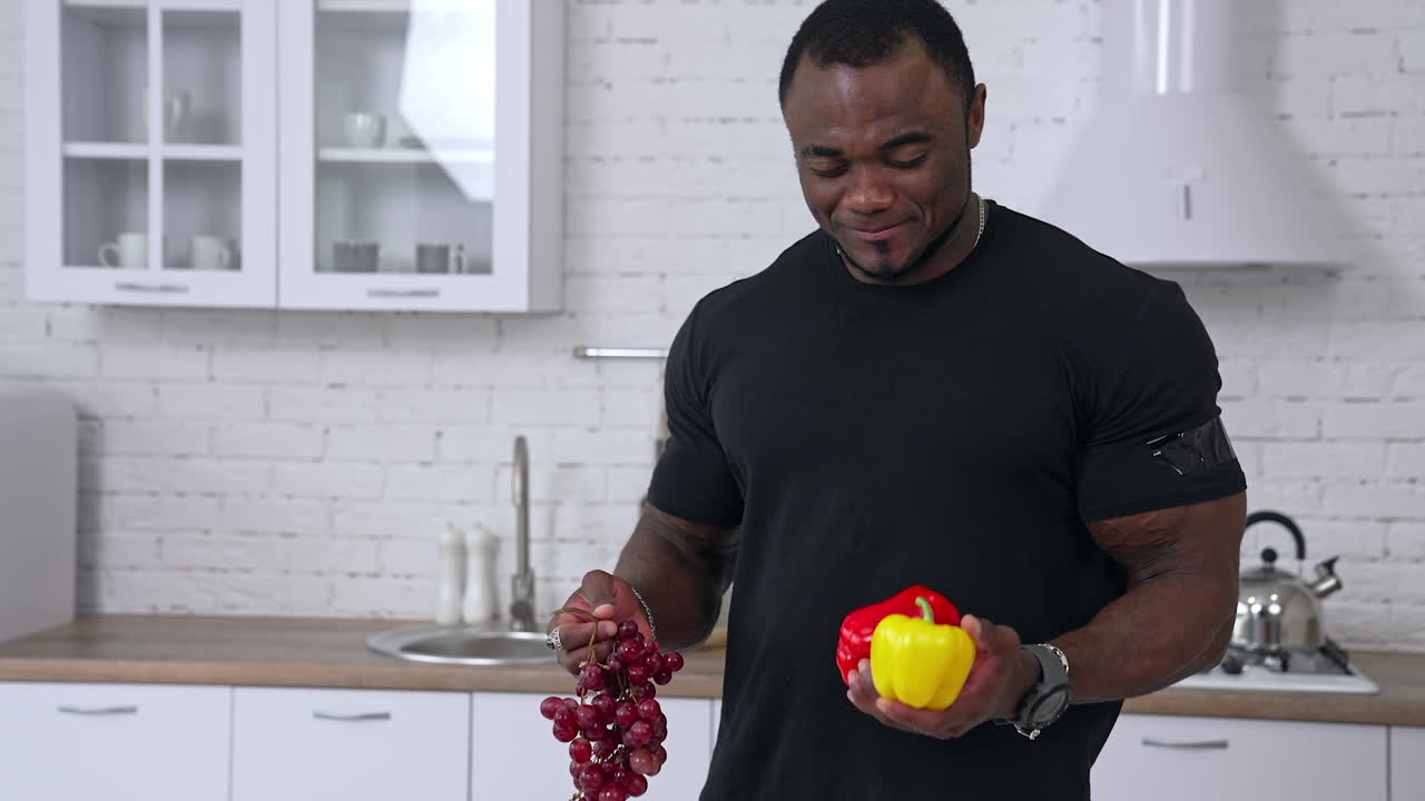 Sporty fit African man in the kitchen. Black male holding fruit and vegetables in his hands. Healthy male offering fresh vegetables.