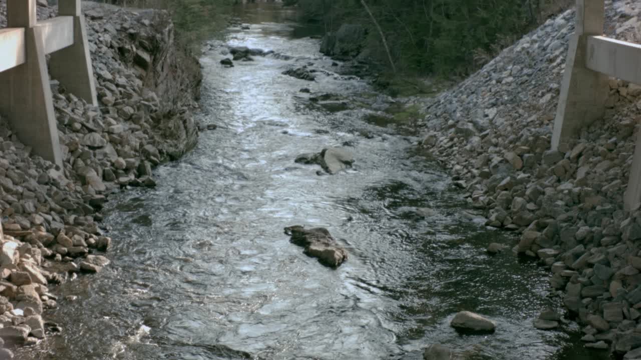Una perspectiva elevada de un río tranquilo que corre entre dos lechos rocosos empinados en la base de un puente