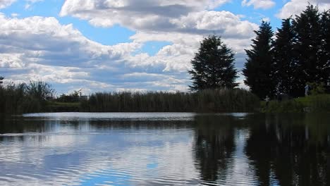 people on banks of blue lake water mirror reflection bright scenic cloudy sky