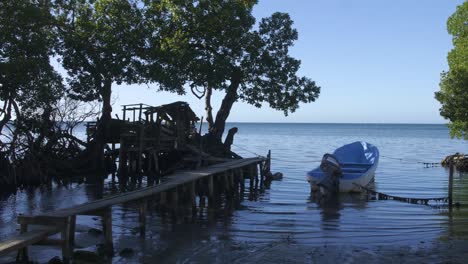 Beach-shore-in-Punta-Gorda,-Roatan,-Honduras-with-a-small-boat-tied-down-and-docked-in-a-household-pier