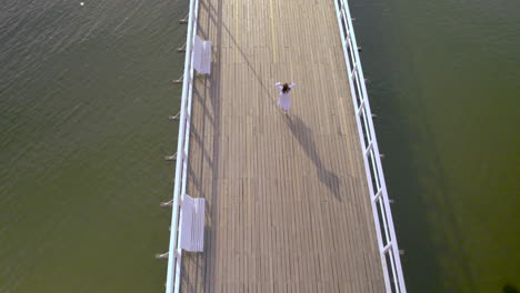 Birds-Eye-View-Of-Women-In-White-Dress-Walking-Across-Wooden-Pier