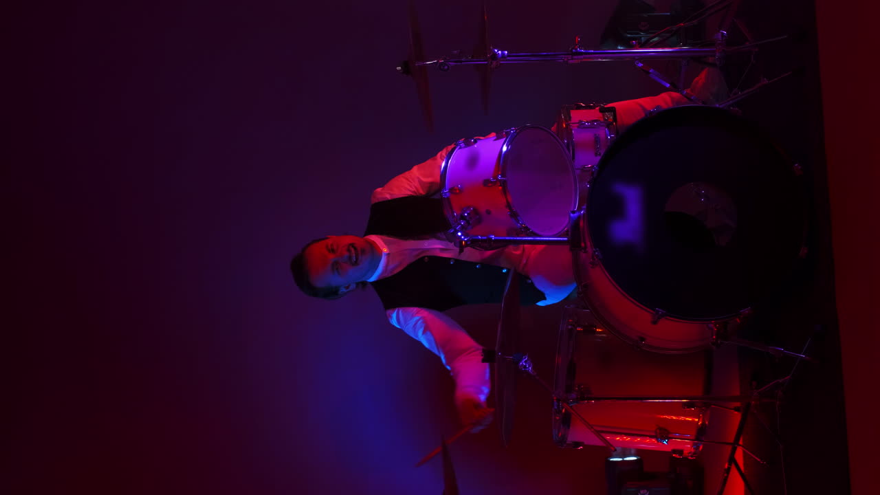 Vertical video bright neon light a male drummer plays in a Studio in neon light and smoke
