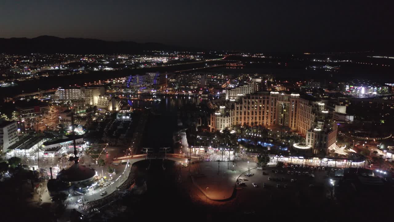 Multiple flashing lights during nightlife in Eilat witht the beautiful lit Queen of Sheba hotel and silhouettes of mountains in the background. Night drone dolly shot