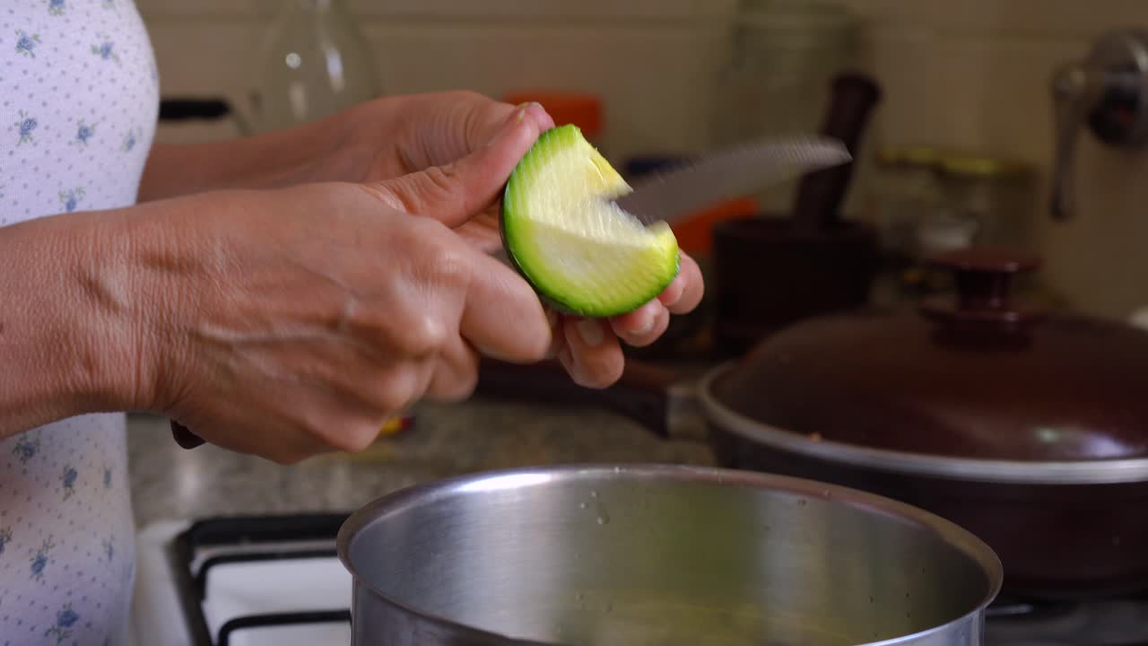 manos femeninas sosteniendo y cortando calabaza verde fresca de verano en la cocina