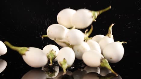 several white thai eggplants fall and bounce on a glossy black surface, captured in slow motion with dramatic studio lighting and high contrast