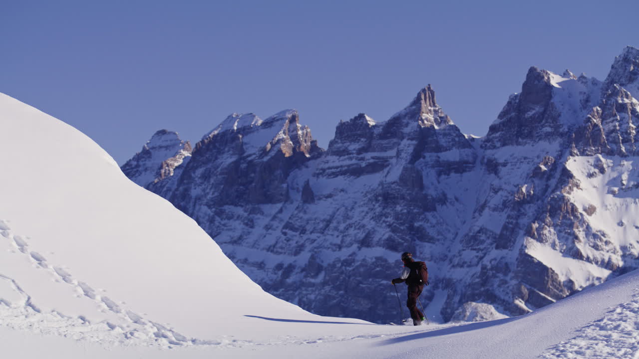 Freeride skier skinning up with Dents du Midi backdrop, then charging steep powder on a bluebird day near Champéry and Avoriaz.