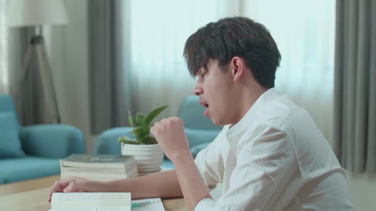 Close Up Of Asian Man Student Being Sleepy While Reading A Book At Home