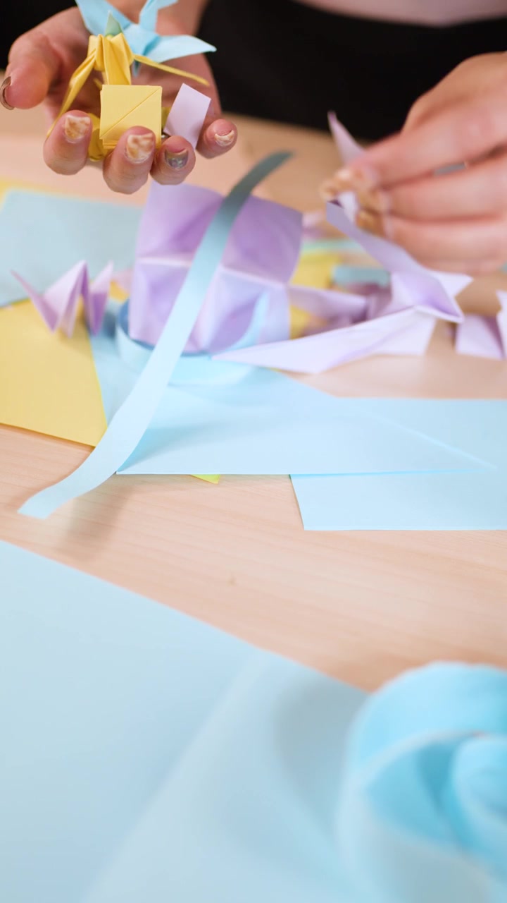 Primo piano di mani che piegano meticolosamente e dispongono origami di carta colorati su un tavolo di legno.