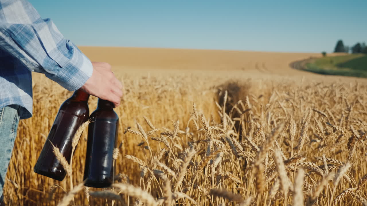 un hombre con dos botellas de cerveza camina por un campo de trigo