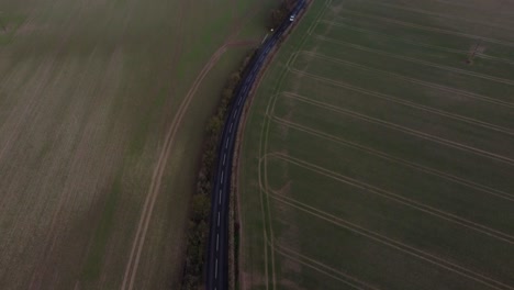 a drone reveal shot showing a beautiful country road with greenfields and open space