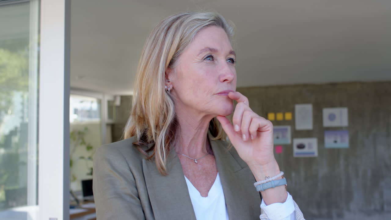 Thinking deeply, senior woman in casual attire with hand on chin indoors, in office