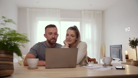 una pareja caucásica sentada en casa resolviendo las finanzas escribiendo en la computadora portátil