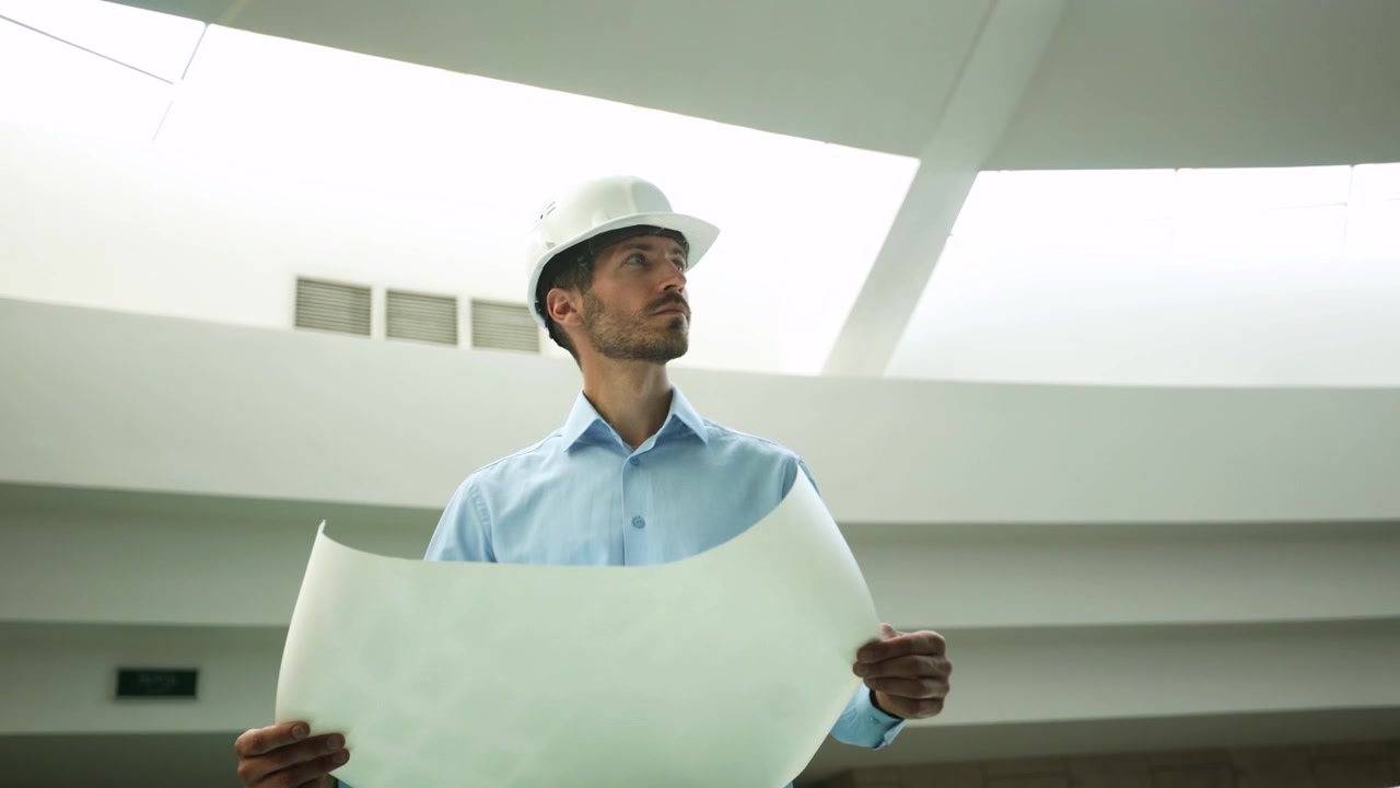 Ingeniero con sombrero inspeccionando planos en un edificio moderno