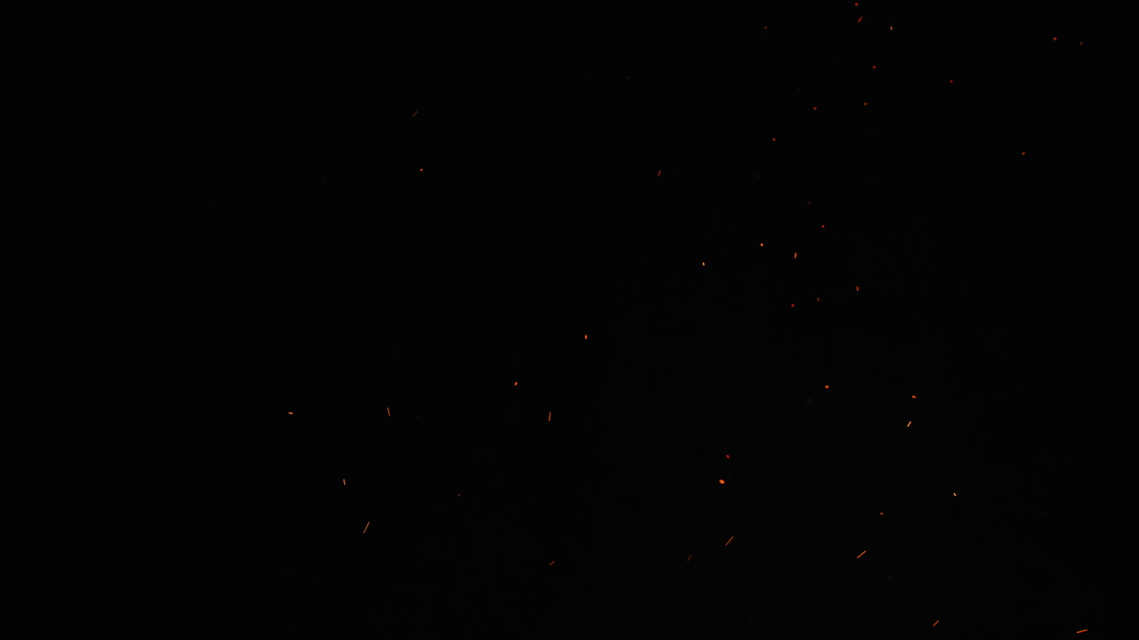 Against a dark black sky, sparks and embers from a large bonfire erupt into the empty space. This clip is ideal for projects related to camping, the outdoors, or travel, or used as an overlay.