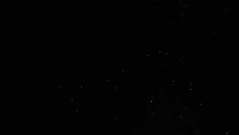 against a dark black sky, sparks and embers from a large bonfire erupt into the empty space. this clip is ideal for projects related to camping, the outdoors, or travel, or used as an overlay.