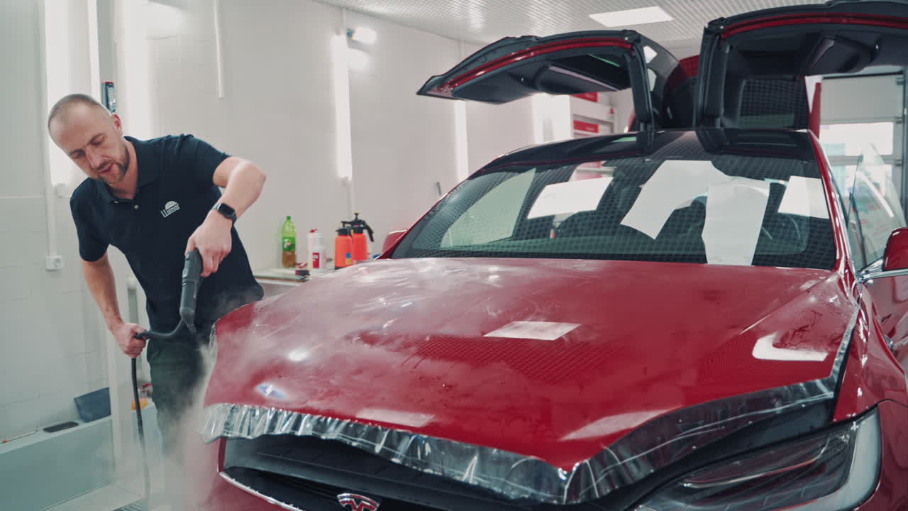 Worker installs car protection film. Car wrapping specialist putting foil on Tesla
