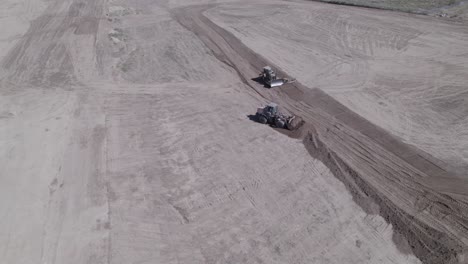 A-drone-observes-a-synchronized-effort-as-a-wheel-loader-and-a-track-loader-work-in-tandem,-flattening-land-for-a-future-home-construction-site