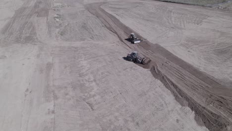 a drone observes a synchronized effort as a wheel loader and a track loader work in tandem, flattening land for a future home construction site