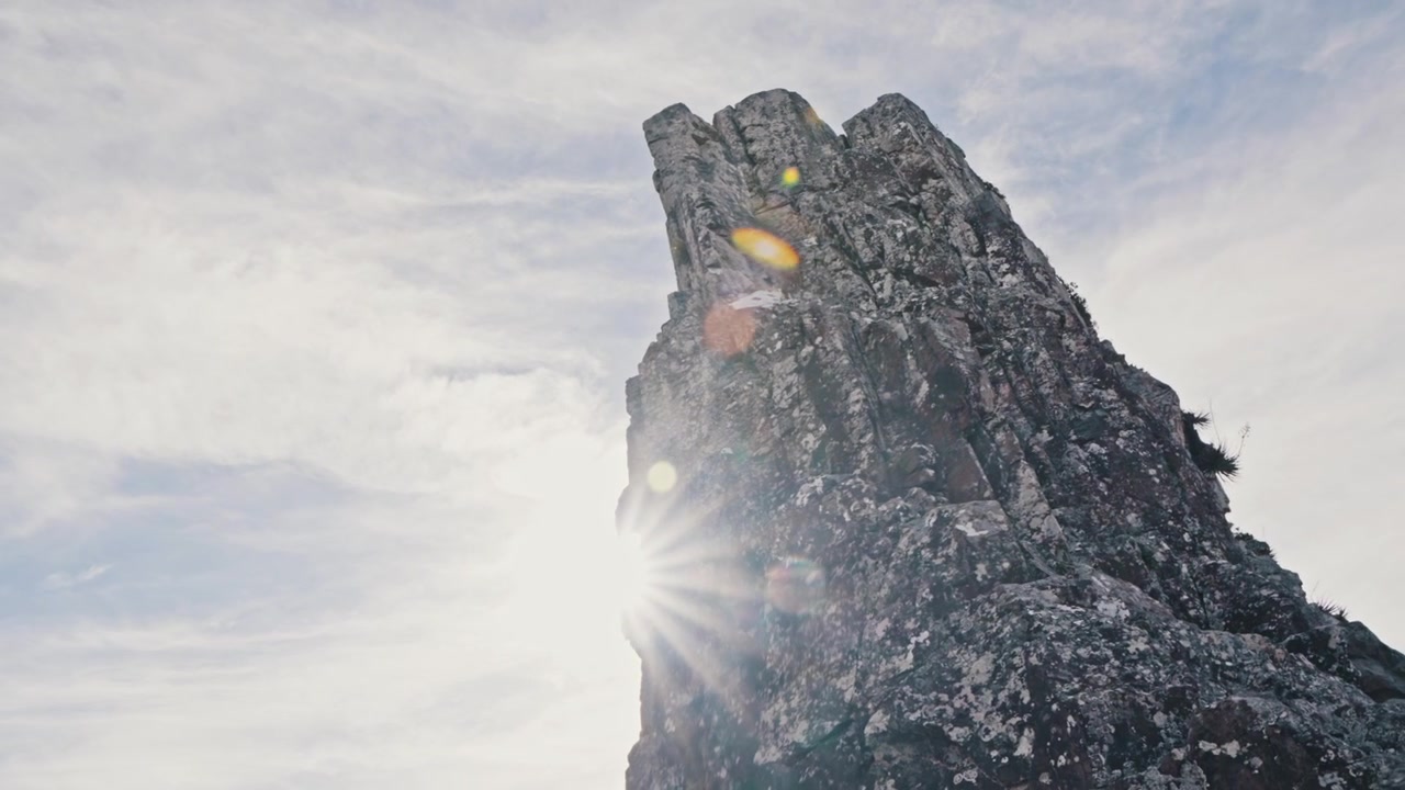 La telecamera si inclina verso il basso da un'imponente formazione rocciosa per rivelare un bagliore solare e una valle di montagna aspra.
