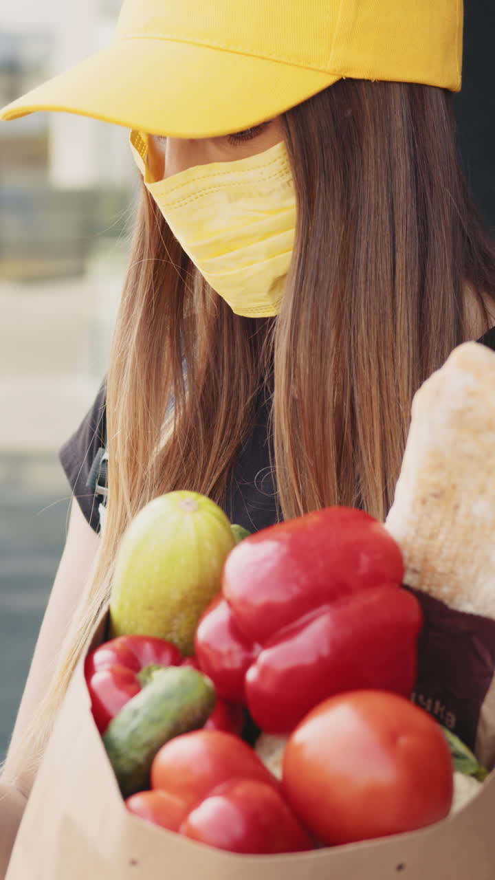 Woman in yellow cap and mask holding a bag of groceries