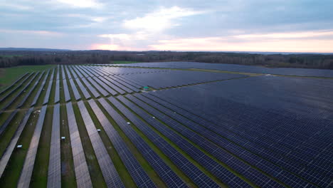 Aerial-establishing-shot-of-solar-panels-farm-on-field-during-sunny-day-with-sun-reflection-on-unit---Alternative-green-energy-concept