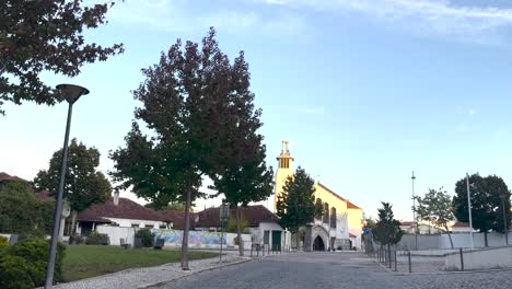 Malerische-Tagesansicht-Einer-Leeren-Straße,-Die-Von-Einem-Mit-Bäumen-Geschmückten-Park-Mit-Spazierwegen-Begrenzt-Wird,-Mit-Einem-Markanten-Religiösen-Kirchengebäude-In-Sichtweite