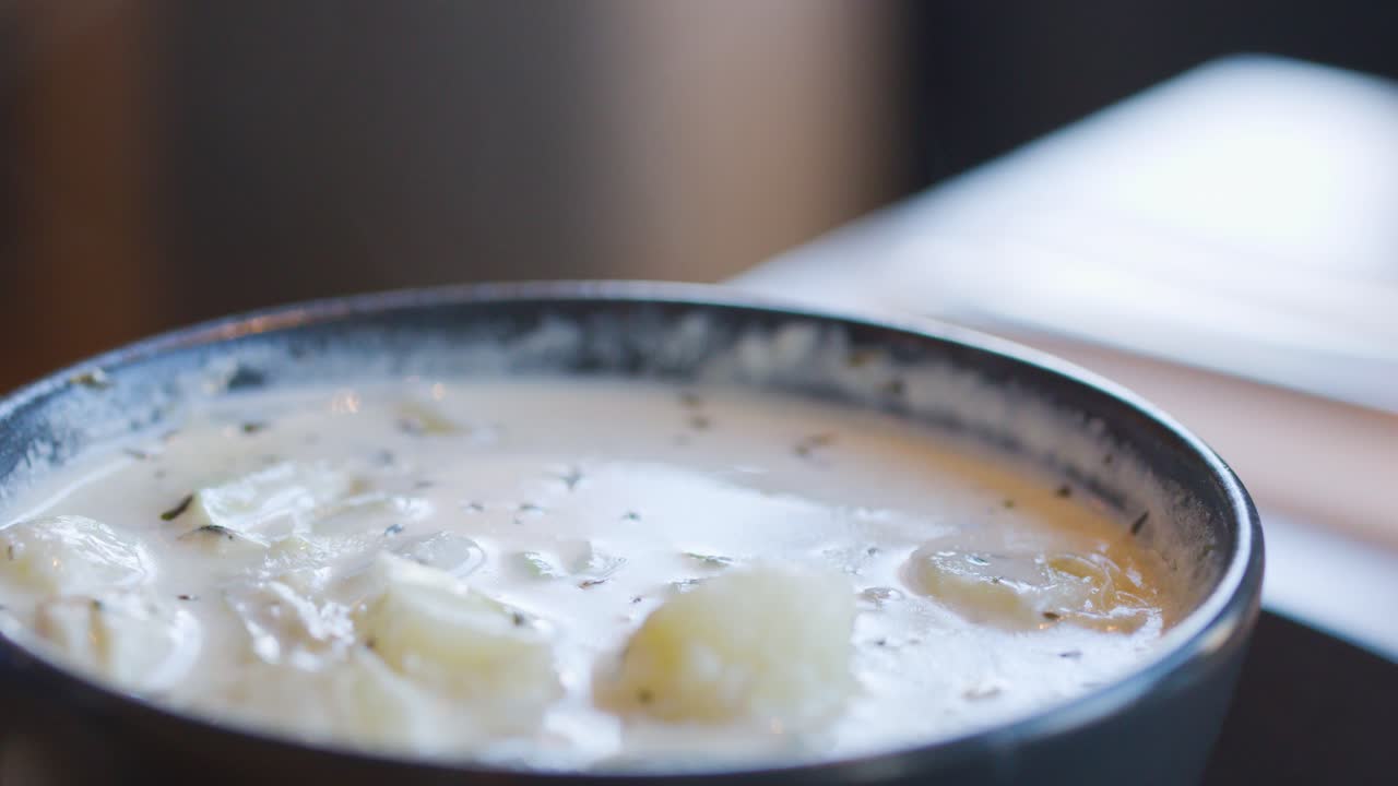 A spoon lifts steaming Cullen skink soup from a rustic bowl, highlighting creamy broth, potatoes, and leeks in soft natural window light