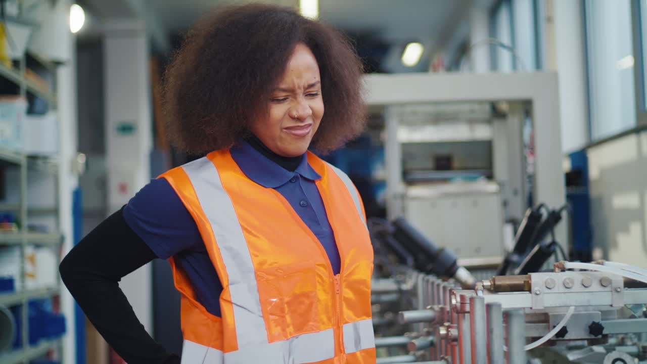 Operaia industriale afroamericana con carico di lavoro fisico e mal di schiena mentre controlla.