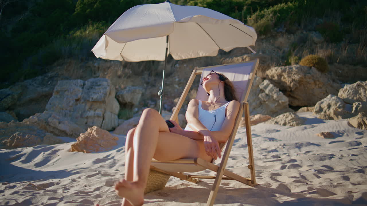 Vacation woman lying beach lounger listening music in headphones. Relaxed female