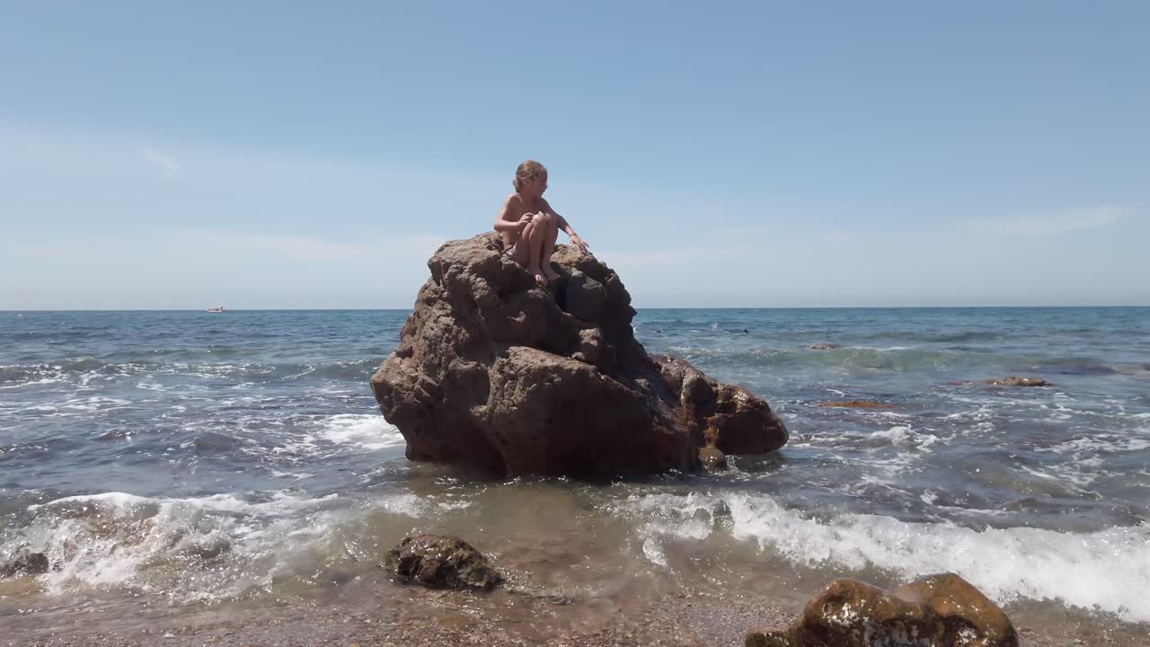 una chica en la cima de una enorme roca en playa de cabo de gata durante el verano en españa
