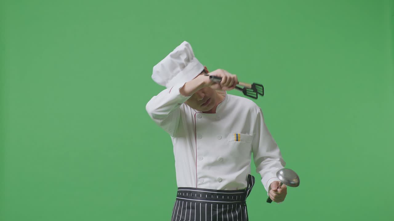 Asian Man Chef Looking At The Tongs And Ladle Wiping The Sweat And Being Tired While Standing In The Green Screen Background Studio