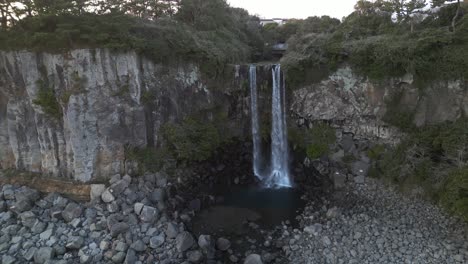 drone aerial view in south korea flying in front of a waterfall over the sea rocky area approach jeju island