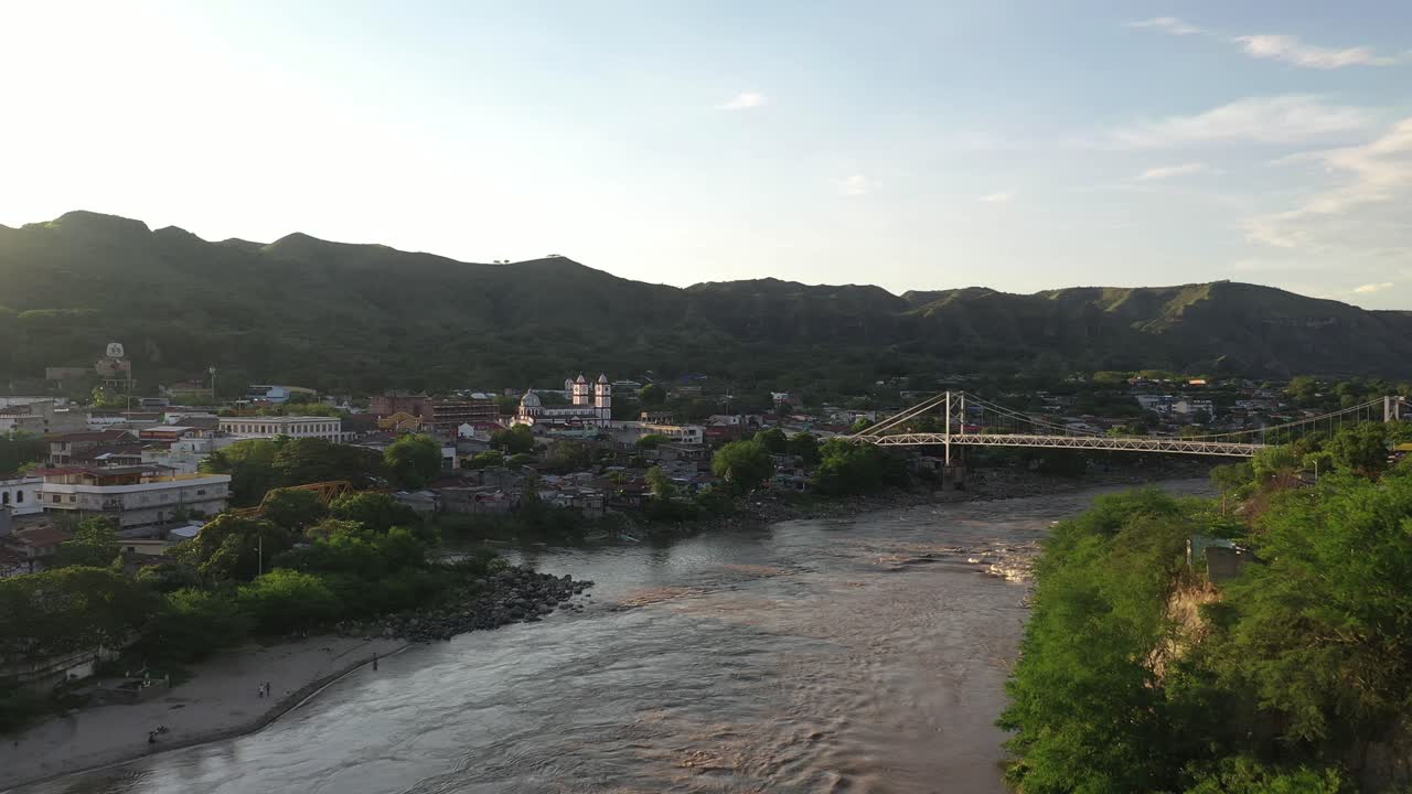 Aerial view, Magdalena river, bridge and Honda town on riverbank at golden hour sunlight, Tolima department of Colombia