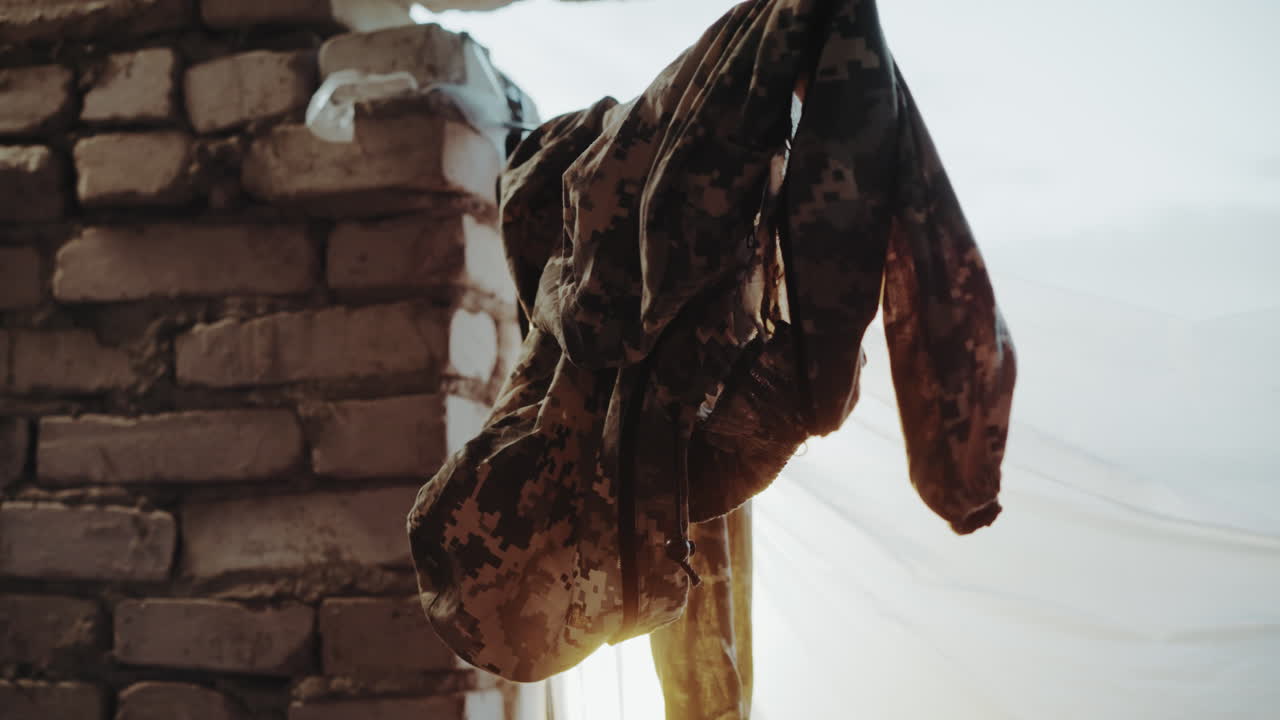 Close up of camouflage cloth hanging on wire indoors near brick wall with sunlight filtering through curtain, fabric folds creating strong texture and moody atmosphere reflecting resilience