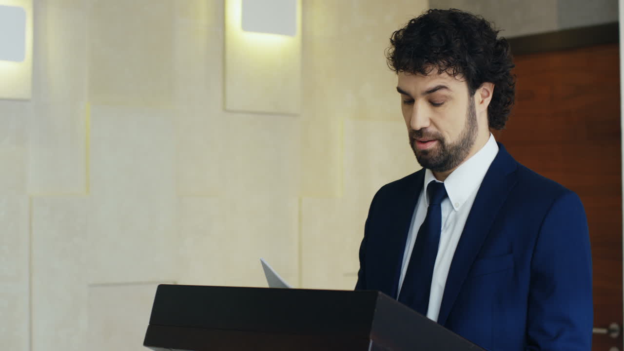 Caucasian businessman speaker on a podium at a conference reading documents and interacting with people in the hall during his speech