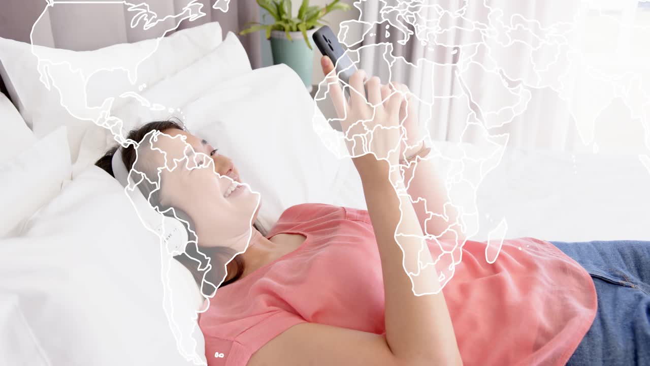 침대에 누워 스마트폰을 두드려 세계 지도 오버레이를 활성화하고 기술 콘텐츠에 반응하는 여성