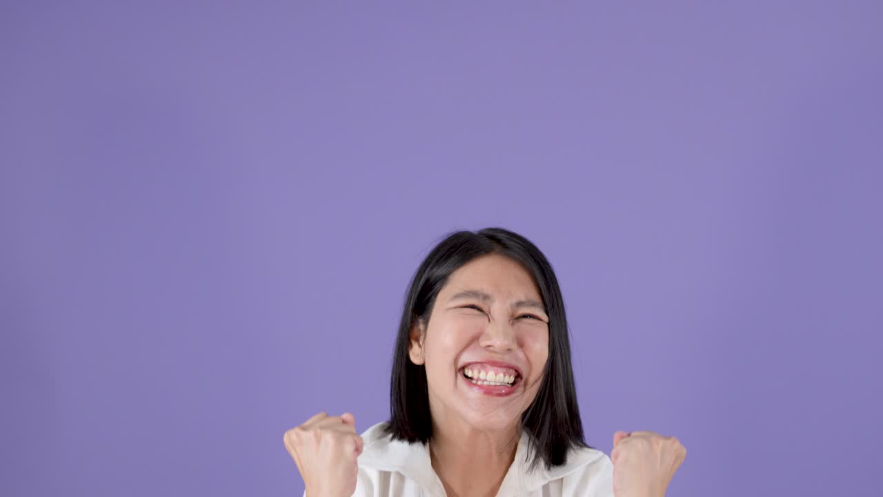 Joyful young woman energetically cheering and jumping with raised arms in bright studio lighting