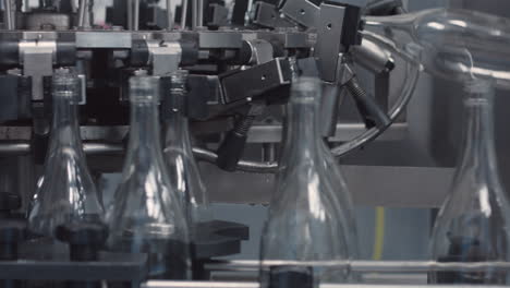 medium shot of glass bottles lined up one by one, descending an industrial production line, ready for the filling process.