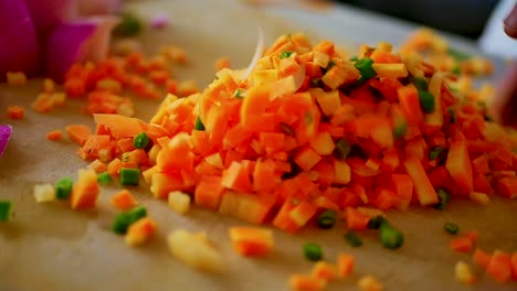 una persona mezclando zanahorias picadas y guisantes con las manos en una tabla de cortar de madera, cerrar
