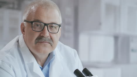 Portrait-of-a-male-doctor-in-a-laboratory-with-a-microscope-looking-at-the-camera.-High-quality-4k-footage