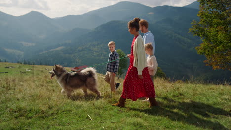 Parents-kids-walking-dog-on-mountain-hill.-Girl-with-mother-holding-husky-leash.