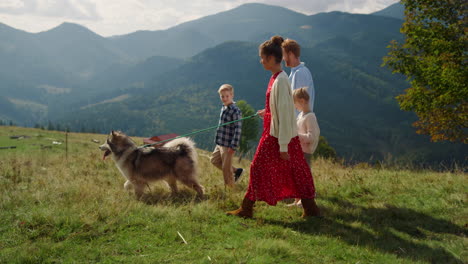 parents kids walking dog on mountain hill. girl with mother holding husky leash.