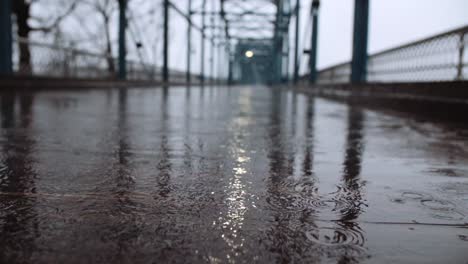 Low-angle-perspective-of-a-footbridge-with-rain-falling-in-the-pedestrian-bridge,-slow-motion-shot